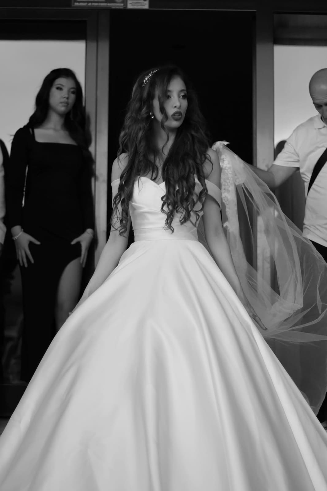 A bride stepping out of a doorway while her party looks on.