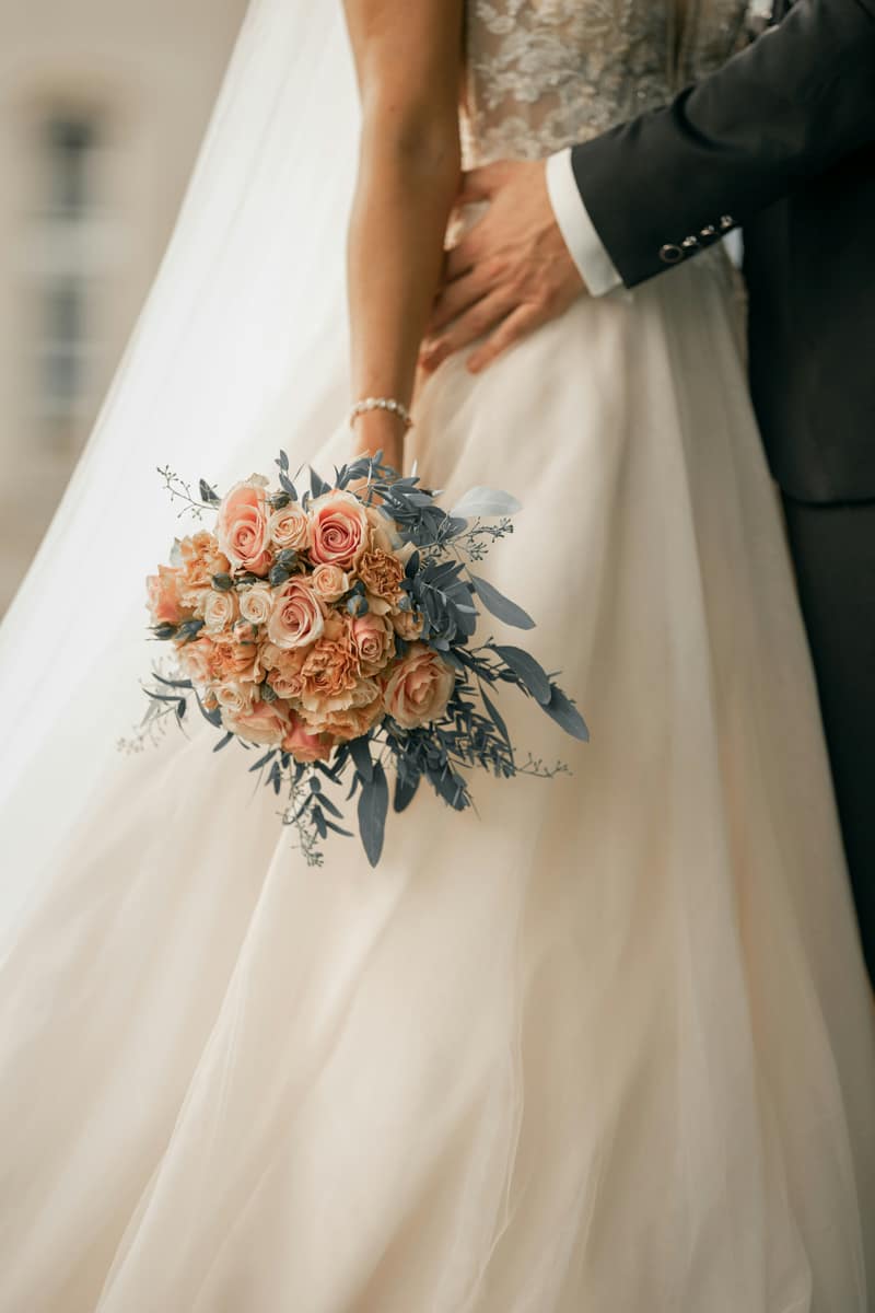 A bridal bouquet of soft peach roses held against the gown